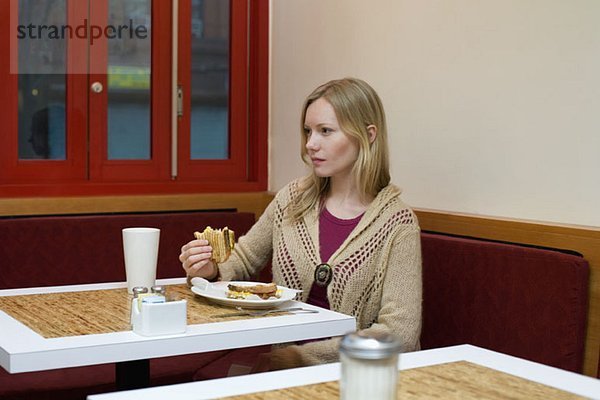 Eine junge Frau sitzt in einem Café und isst ein getoastetes Sandwich.