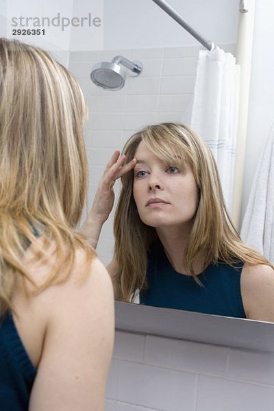 Eine junge Frau  die in einen Badezimmerspiegel schaut.