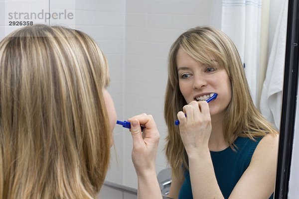 Eine junge Frau beim Zähneputzen vor einem Badezimmerspiegel