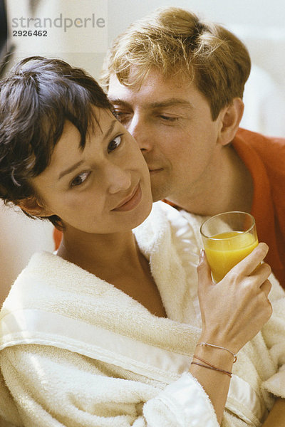 Frau hält ein Glas Orangensaft  der Mann küsst ihre Wange.