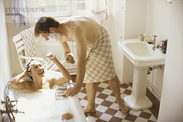 Paar im Bad  Frau in der Badewanne  Mann lehnt sich über sie mit Rasiercreme im Gesicht