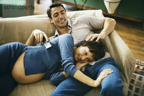 Erwartendes Paar  das sich auf dem Sofa entspannt  fernsieht  Frau  die den Kopf auf dem Schoß des Mannes ausruht.