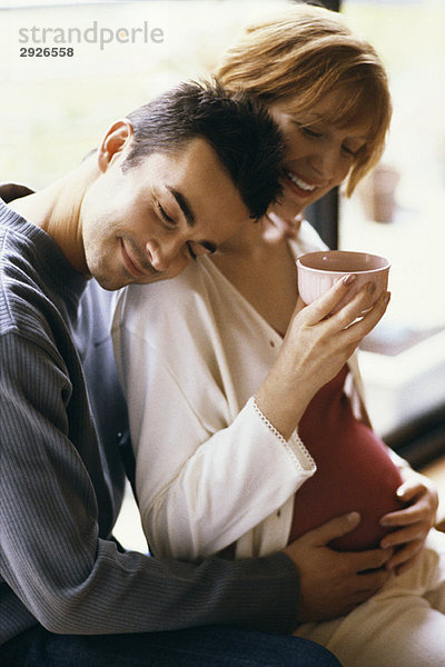 Mann umarmt schwangere Frau  Hände auf dem Bauch  Frau trinkt Tee