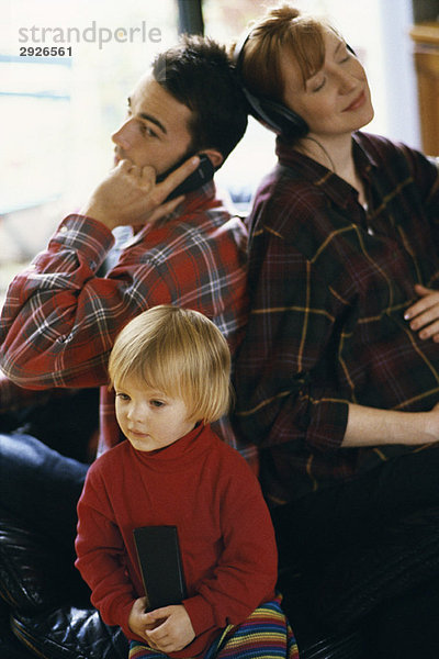 Familie sitzt Rücken an Rücken  Vater benutzt Handy  Mutter hört Kopfhörer  Tochter schaut TV