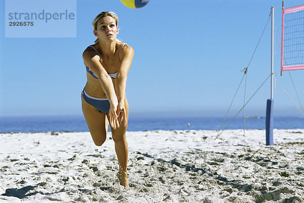Eine Frau spielt Beachvolleyball  um den Ball zu fangen.