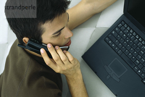 Mann telefoniert  stützt sich auf den Ellenbogen  benutzt einen Laptop