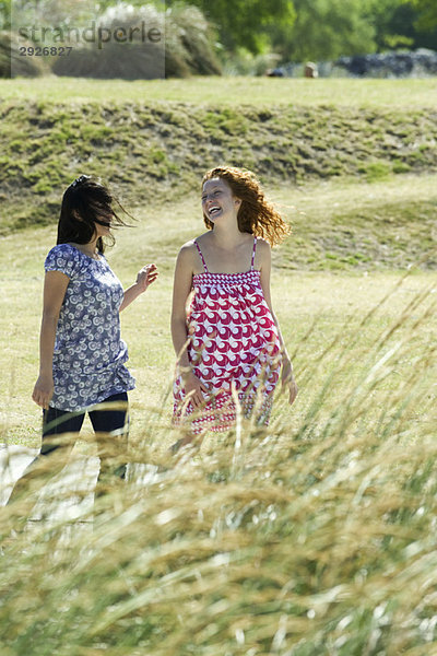 Zwei junge Frauen  die gemeinsam im Freien spazieren gehen und lachen.