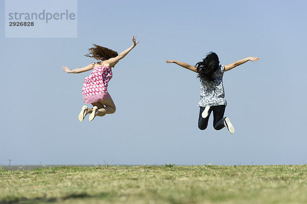 Zwei junge Frauen beim Springen im Freien  Rückansicht