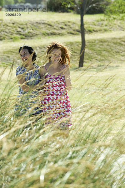 Zwei junge Frauen lachen gemeinsam im Freien  hohes Gras im Vordergrund