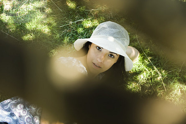 Junge Frau mit Sonnenhut auf dem Boden liegend  Blick in die Kamera  selektive Fokussierung