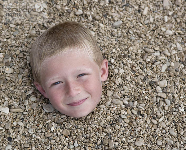 Junge in Kieselsteinen am Strand begraben