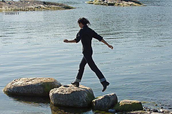 Junge Frau springen auf Steine im Wasser Schweden.