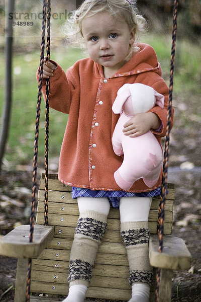 Portrait von little mädchen mit blond lockiges Haar stehend auf Swing.