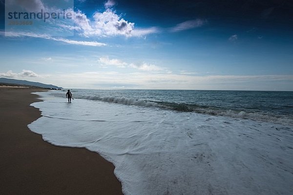 Junge Mann zu Fuß entlang der Küstenlinie mit seinem Surfbrett