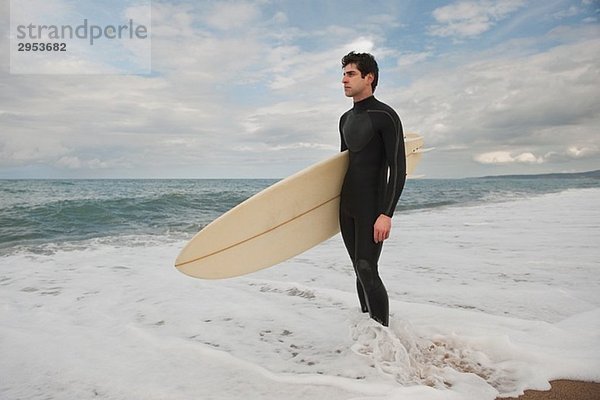Surfer stehen an Uferlinie und Surfbrett unter seinem Arm hält
