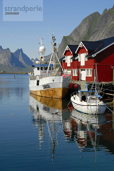 Blick über den Fjord mit Booten und Fischerhäusern  Rorbuer (Rorbu) Häuser auf die Berge von Moskenesoya  Reine  Hamnöy  Lofoten  Norwegen  Skandinavien
