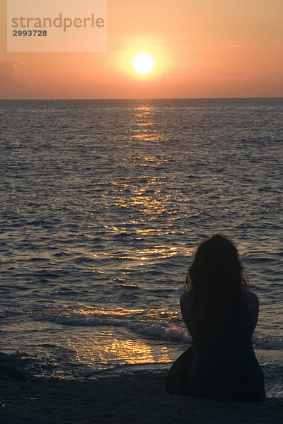 Frau beobachtet den Sonnenuntergang am Strand