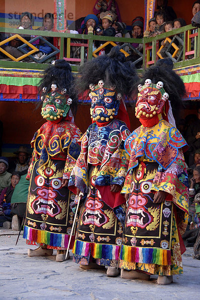 Drei Mönche tragen schreckliche bunte Masken und Gewänder von Dämonen vor vielen tibetischen Pilgern bei Festival in bunt geschmücktem Kloster Rongbuk Tibet China