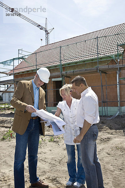 Paar unterhält sich mit einem Architekt auf einer Baustelle