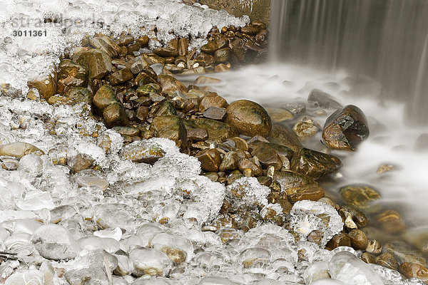 Steine an einem Wasserfall sind mit einer Eisschicht überzogen