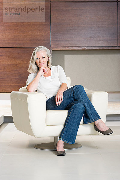 Porträt einer Frau mittleren Alters  die auf einem modernen Sessel sitzt.