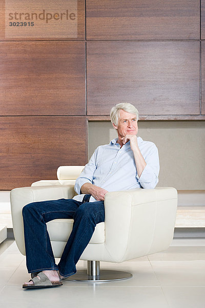 Nachdenklicher Mann mittleren Alters sitzt auf einem modernen Sessel.