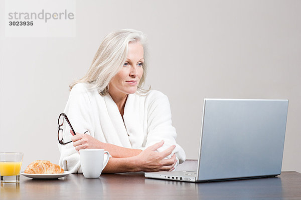 Frau mittleren Alters sitzend am Frühstückstisch mit Laptop