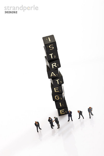 Gestapelte Scrabble-Fliesen als Einzelwortstrategie  im Vordergrund Geschäftsmännerfiguren  erhöhte Ansicht