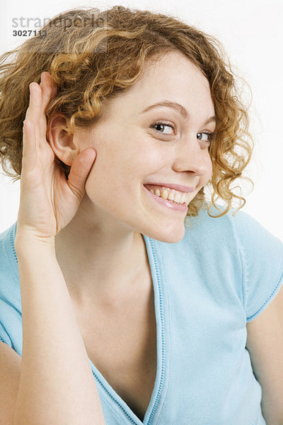 Junge Frau legt Hand an Ohr  lächelnd  Portrait