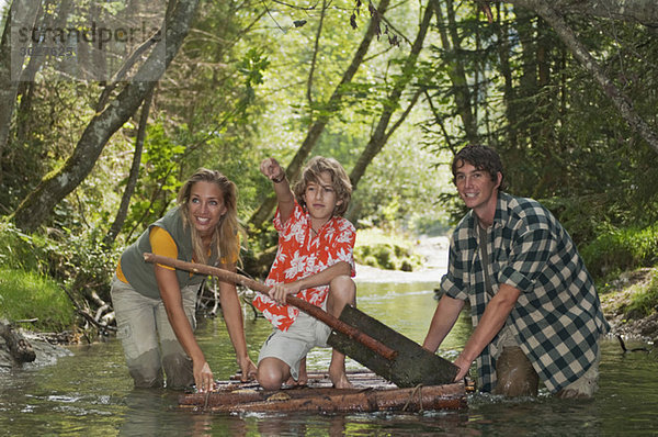 Austria  Salzburger Land  Boy kneeling on timber raft  Parents wading in creek