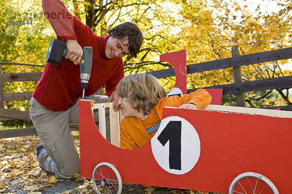 Austria  Salzburger Land  Young man fixing soapbox car  boy (12-13) watching