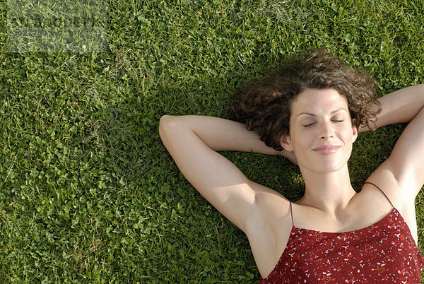 Junge Frau auf Rasen liegend  Augen geschlossen  lächelnd  erhöhte Ansicht  Portrait