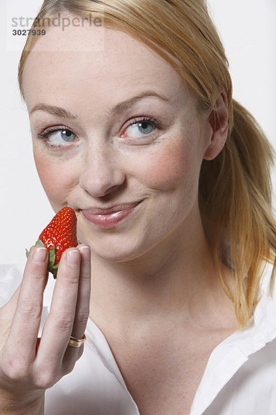 Junge Frau hält Erdbeere  lächelnd  Portrait