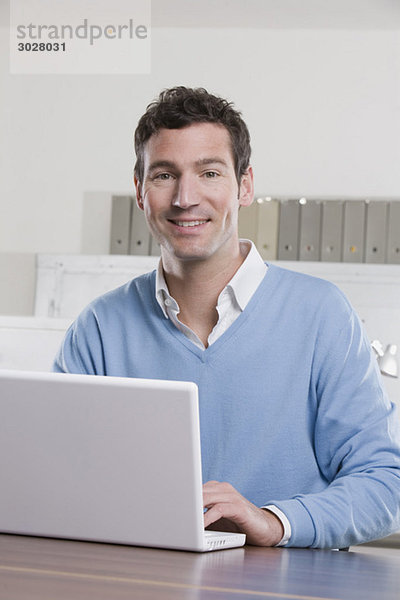 Geschäftsmann im Büro mit Laptop  lächelnd  Portrait