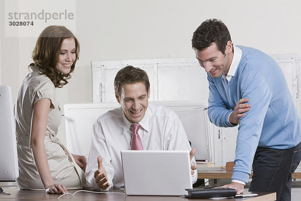 Germany  Munich  co-workers together in office  watching laptop
