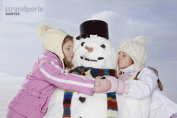 Zwei Mädchen (4-5) (8-9) küssen Schneemann  Augen zu  Portrait