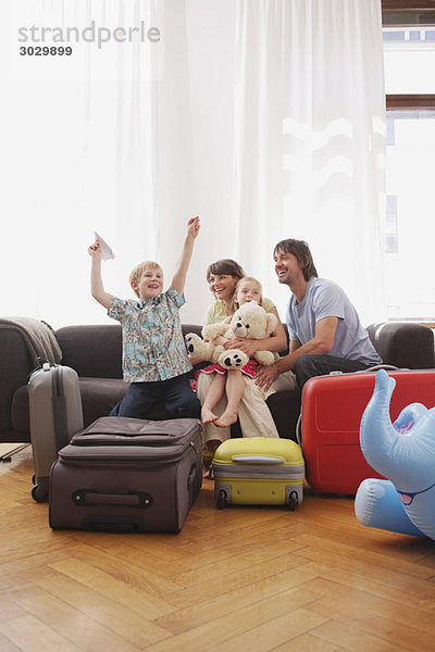 Familie auf Sofa sitzend  Junge (8-9) hält Papierflugzeug  lacht