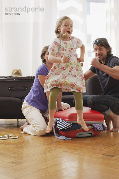 Mädchen (4-5) springend  Vater und Mutter packen Koffer im Hintergrund