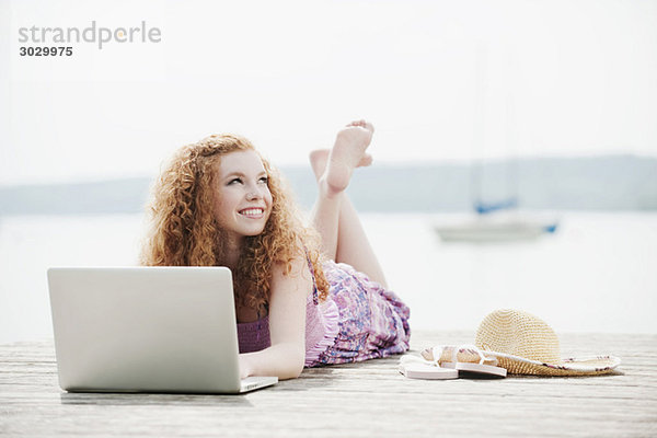 Junge Frau am Steg liegend mit Laptop  Portrait