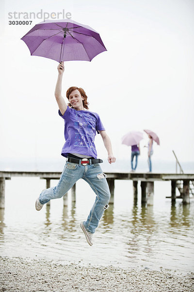 Junger Mann mit Regenschirm und Springen