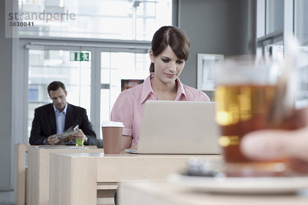 Junge Frau im Cafe mit Laptop  Mann im Hintergrund
