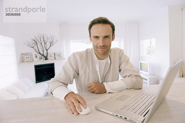 Porträt eines Mannes  der an einem Laptop arbeitet und lächelt