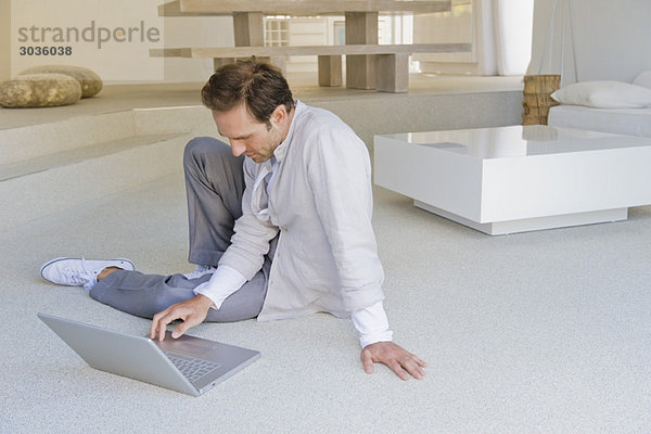 Mann sitzt auf dem Boden und arbeitet am Laptop