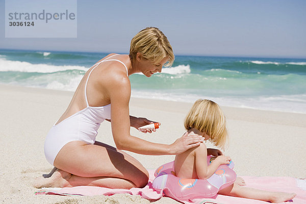 Frau  die Sonnencreme auf ihre Tochter am Strand aufträgt.