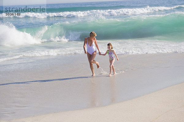 Frau  die mit ihrer Tochter am Strand rennt