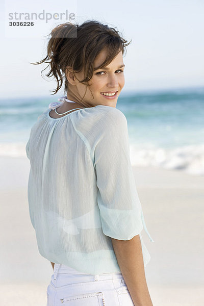 Frau am Strand stehend und lächelnd