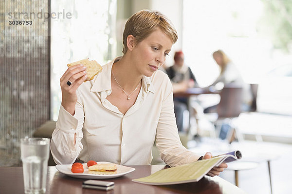 Geschäftsfrau sitzt in einem Restaurant und liest eine Zeitschrift.