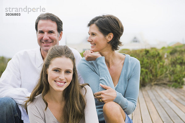 Frau sitzt mit ihren Eltern auf einer Strandpromenade
