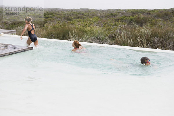 Zwei Mädchen schwimmen in einem Infinity-Pool mit einem Jungen.