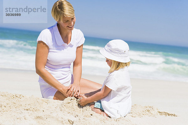 Frau sitzend mit ihrer Tochter am Strand